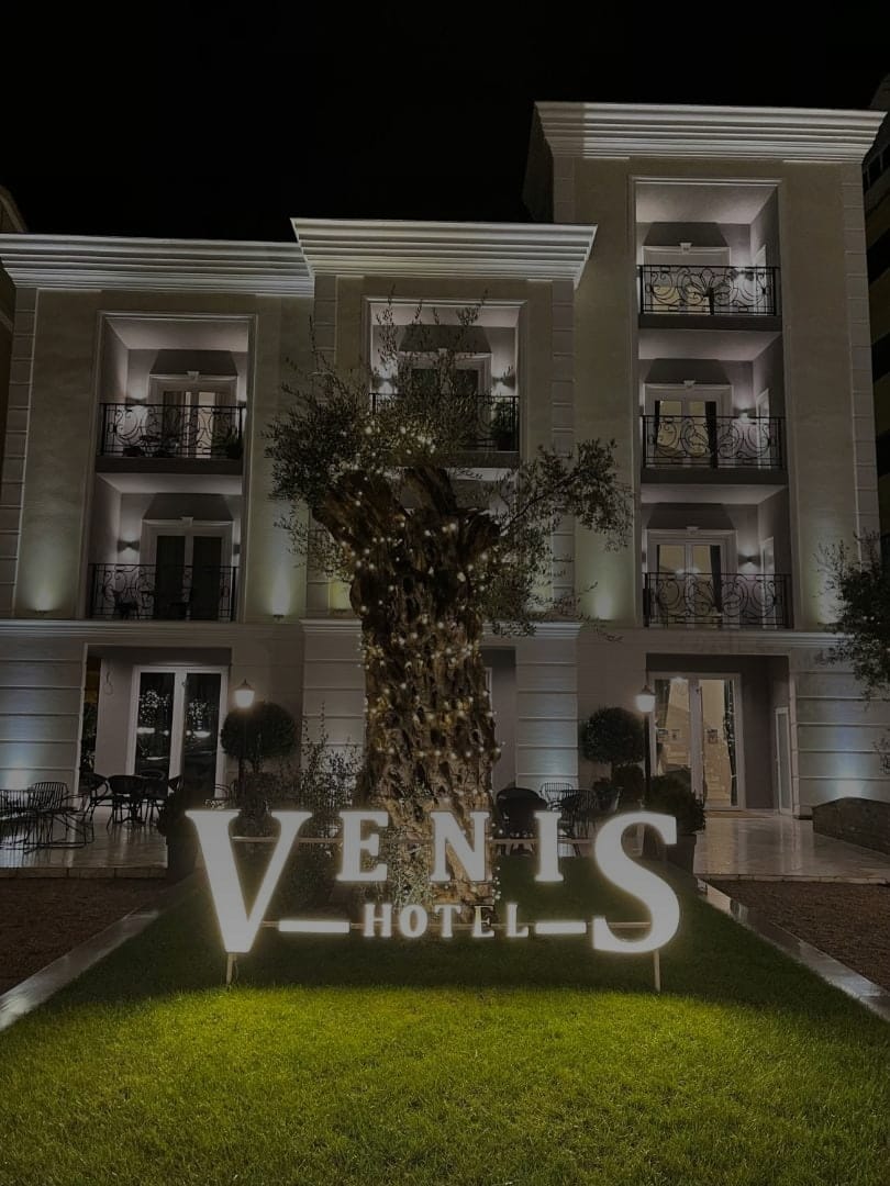 The hotel façade lit at night, with the olive tree